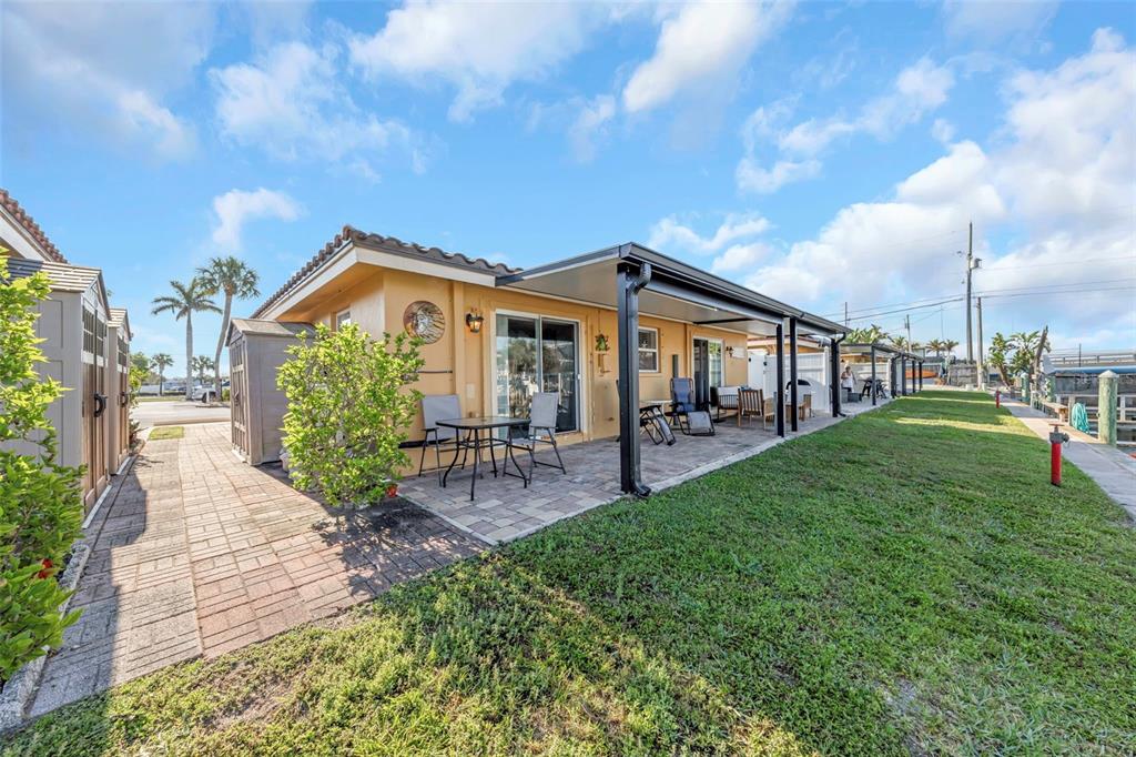 A yellow house with a covered patio, brick pavers, and a grassy yard near water — 2600 N PAULA DRIVE UNIT 12D, DUNEDIN, FL