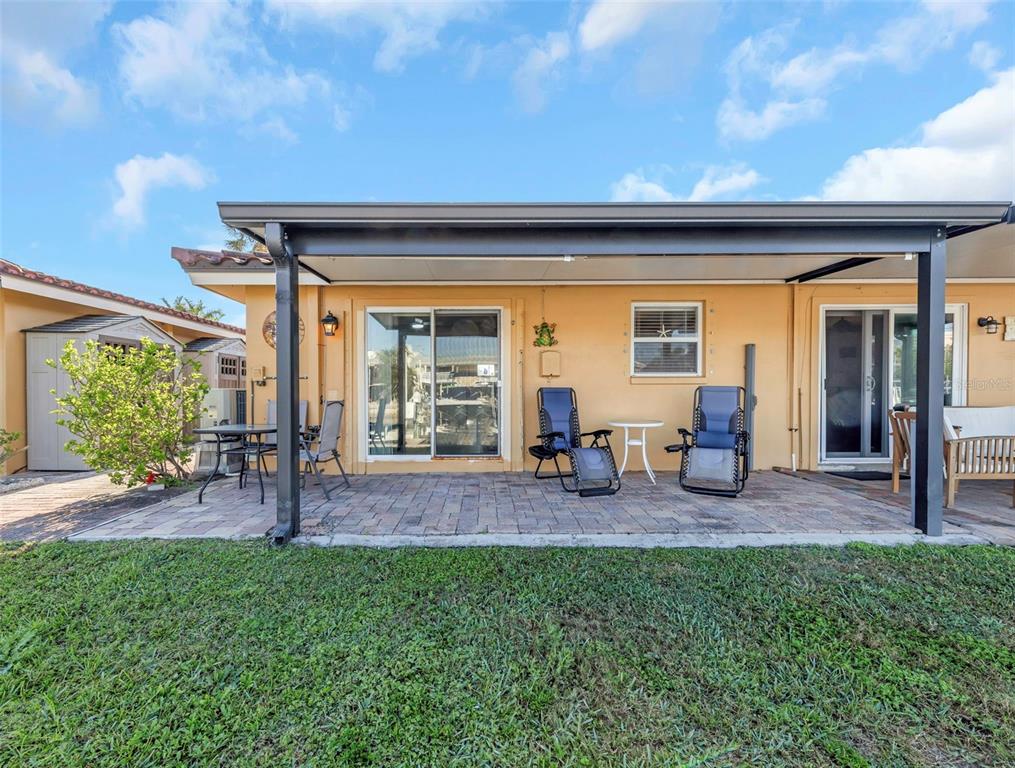 A paved patio with a covered roof sits behind a house with yellow walls — 2600 N PAULA DRIVE UNIT 12D, DUNEDIN, FL