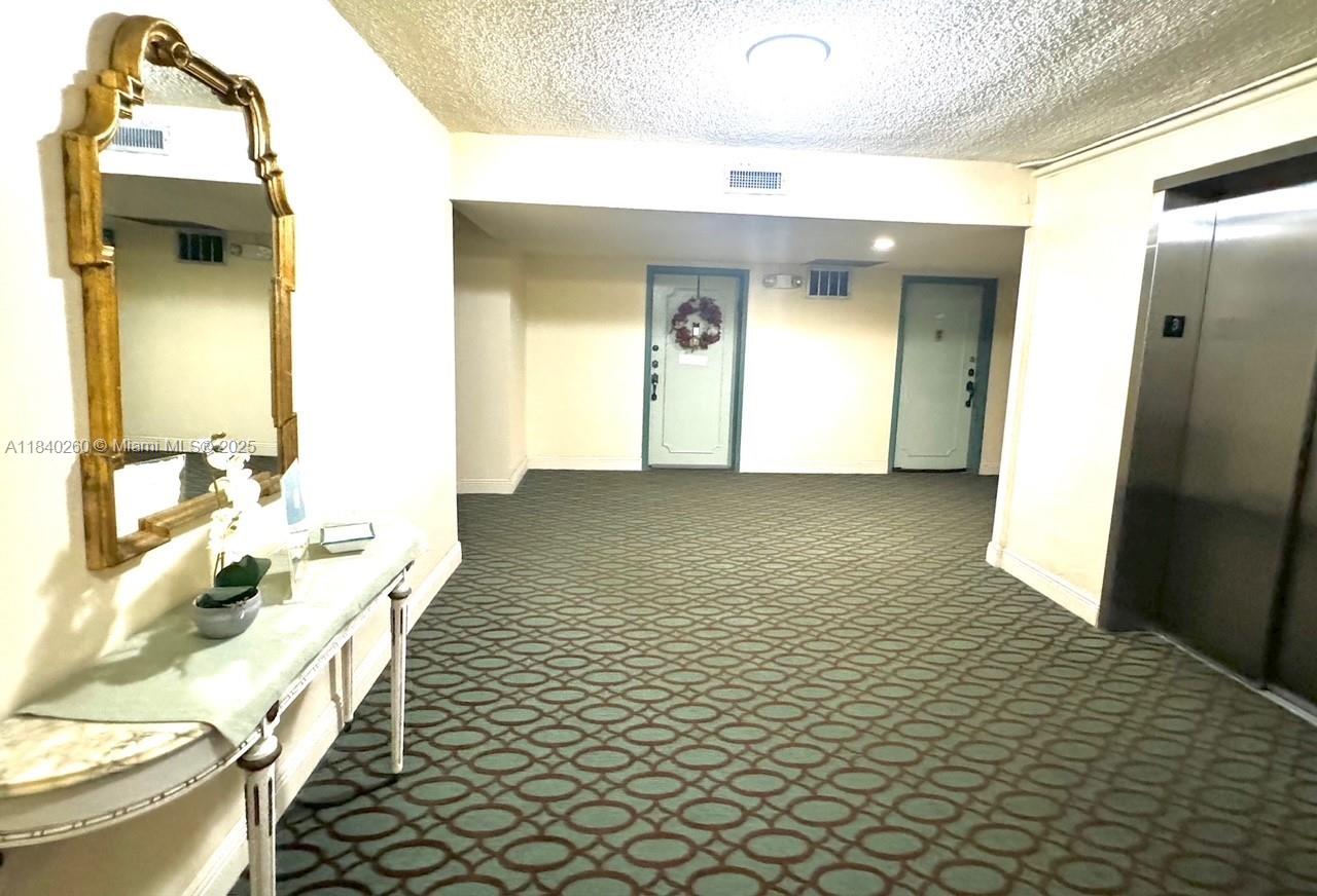 A carpeted apartment building hallway features an elevator, two doors, and a decorative console table — 6911 SW 147th Ave # 3C, Miami FL 33193, MIAMI, FL