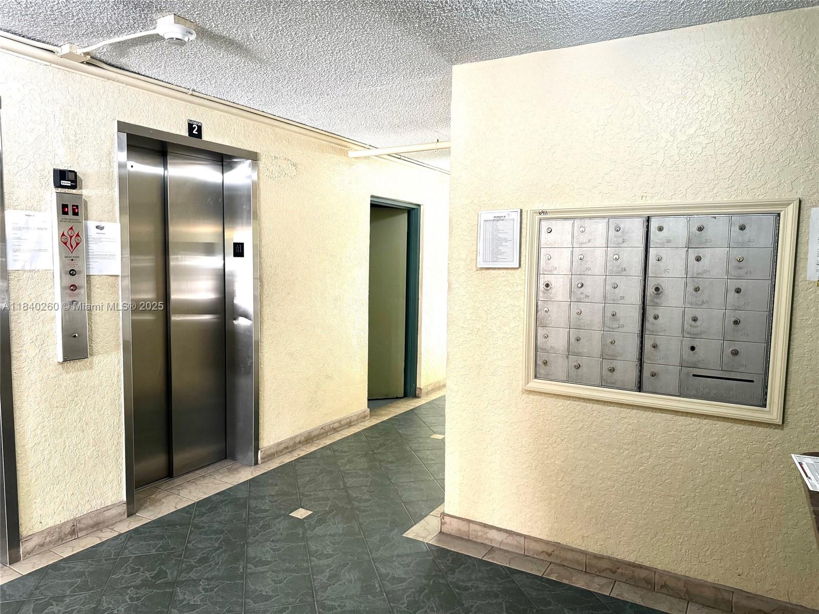 An indoor hallway features an elevator, a doorway, and a wall-mounted bank of mailboxes — 6911 SW 147th Ave # 3C, Miami FL 33193, MIAMI, FL