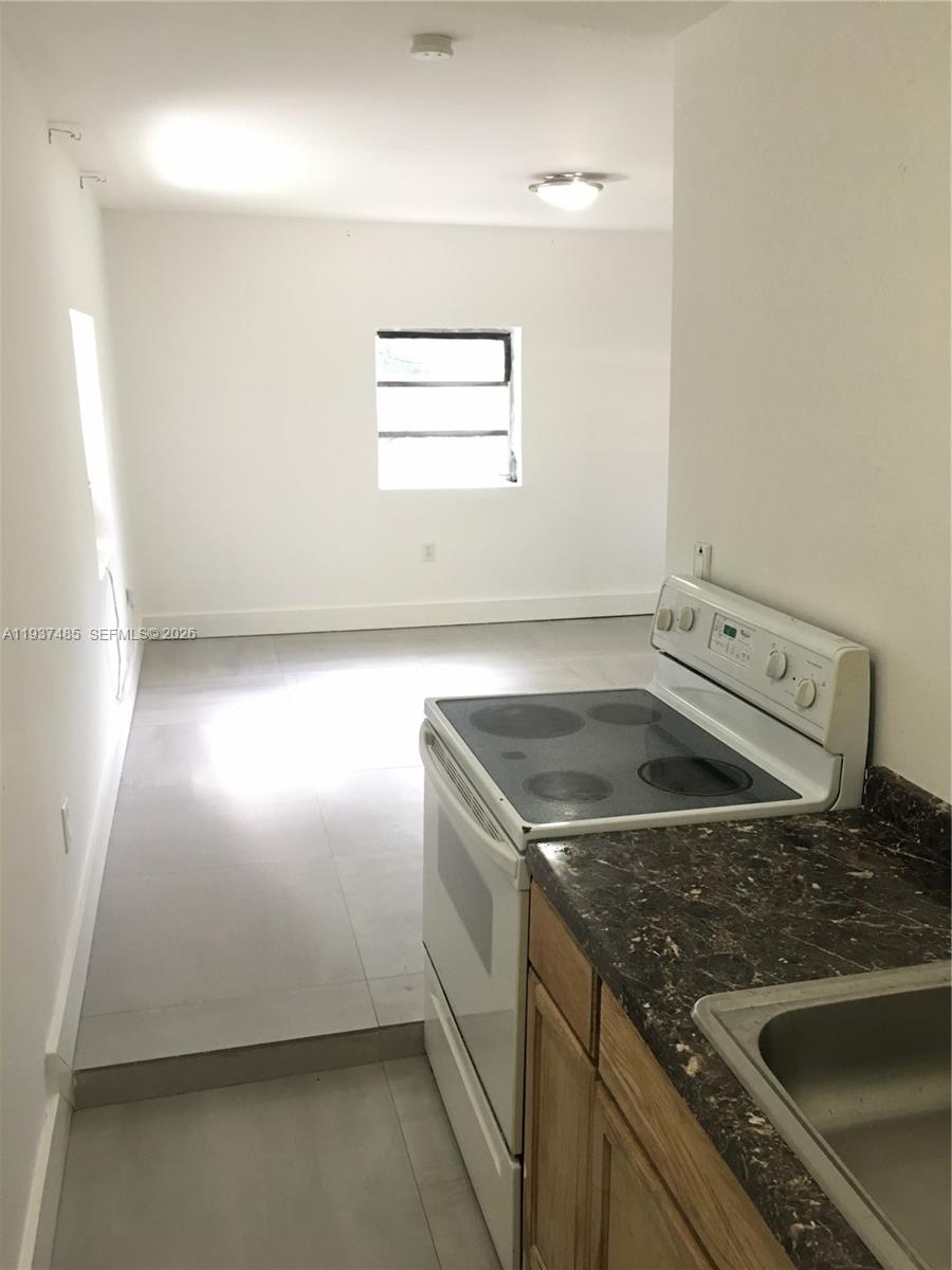 A kitchen with a white electric stove and dark countertop overlooks an adjacent living area — 2612 NE 206th St, Miami FL 33180, MIAMI, FL