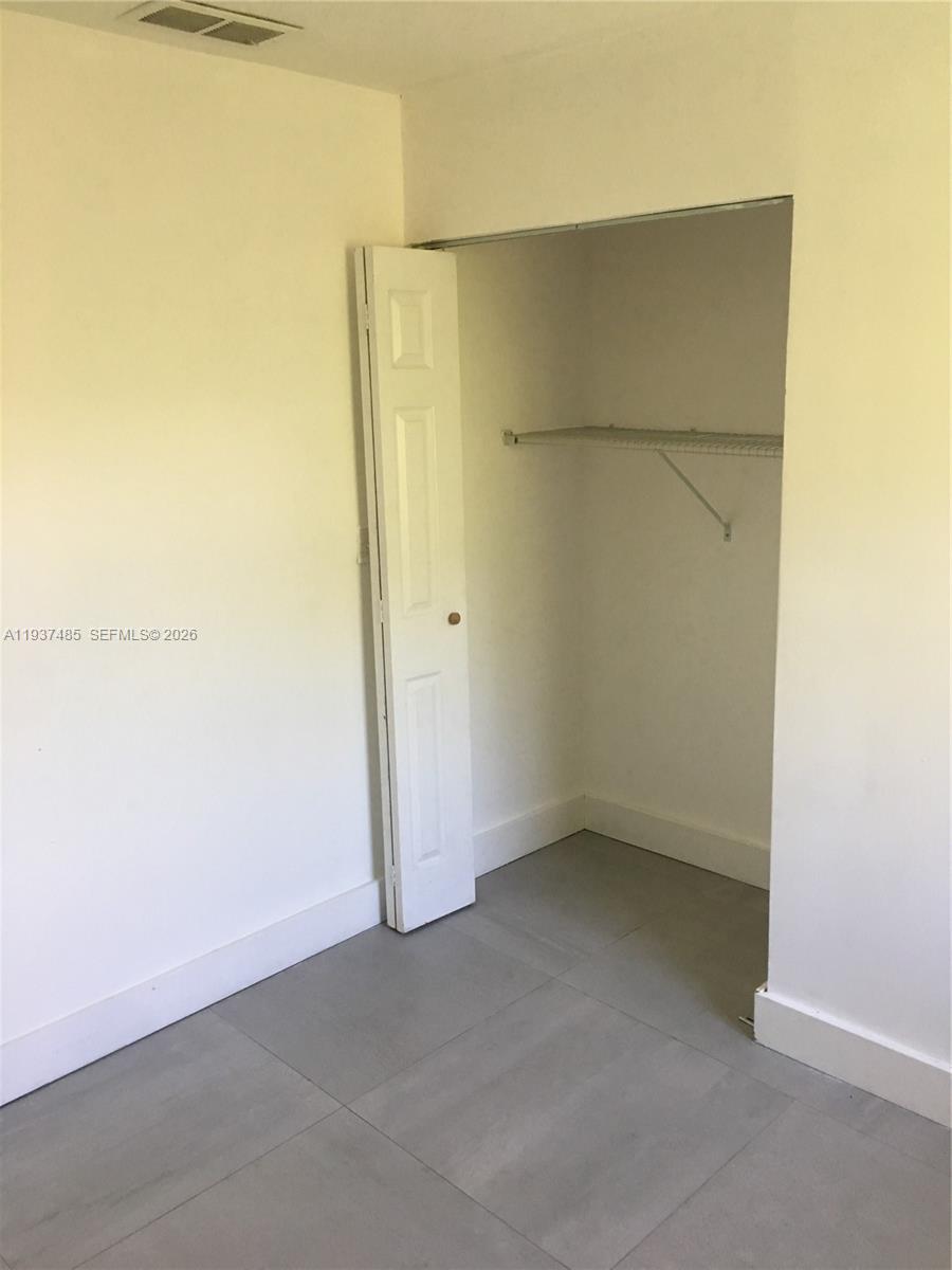A room with light-colored walls, gray tile flooring, and an open closet with shelving — 2612 NE 206th St, Miami FL 33180, MIAMI, FL