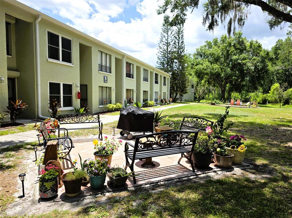 A patio with benches and potted plants sits outside a multi-story apartment building — 1761 CUPECOY CIRCLE UNIT N4, LUTZ, FL