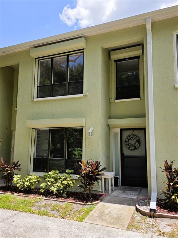 A two-story light green stucco townhouse features dark-framed windows with exterior shutters and a front door — 1761 CUPECOY CIRCLE UNIT N4, LUTZ, FL