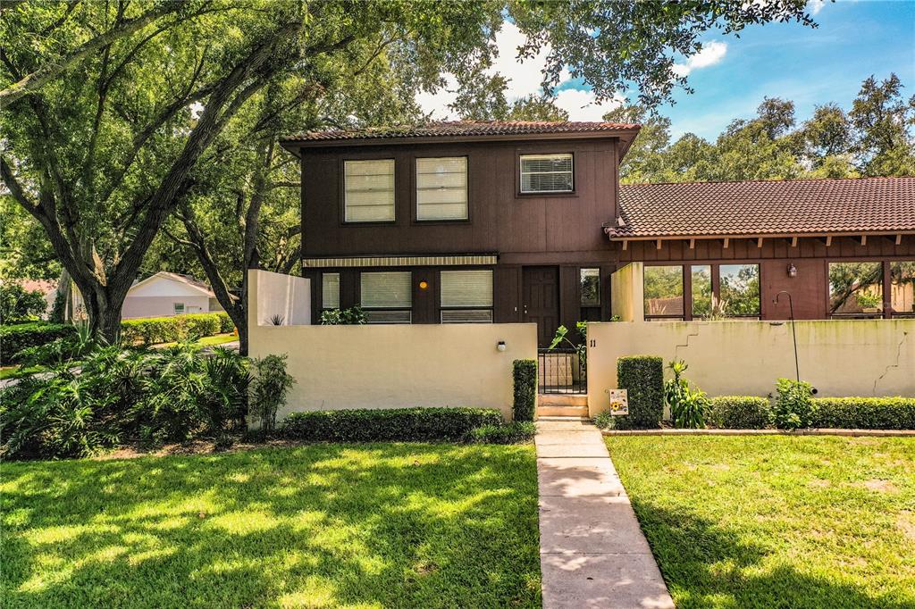 A two-story townhouse with brown wood siding, a tiled roof, and a front courtyard wall — 11 LOMA VERDE UNIT 11, LAKELAND, FL