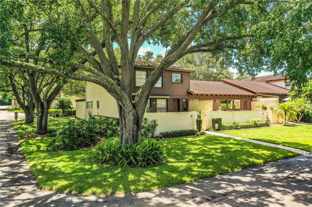 A two-story house with brown wood siding and a stucco wall stands behind large trees — 11 LOMA VERDE UNIT 11, LAKELAND, FL
