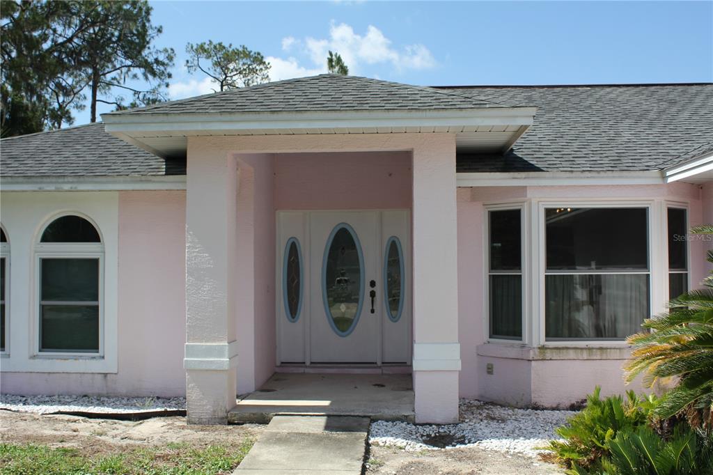 A pink house exterior features a covered entryway with a white door and arched windows — 122 QUAILWOOD DRIVE, WINTER HAVEN, FL