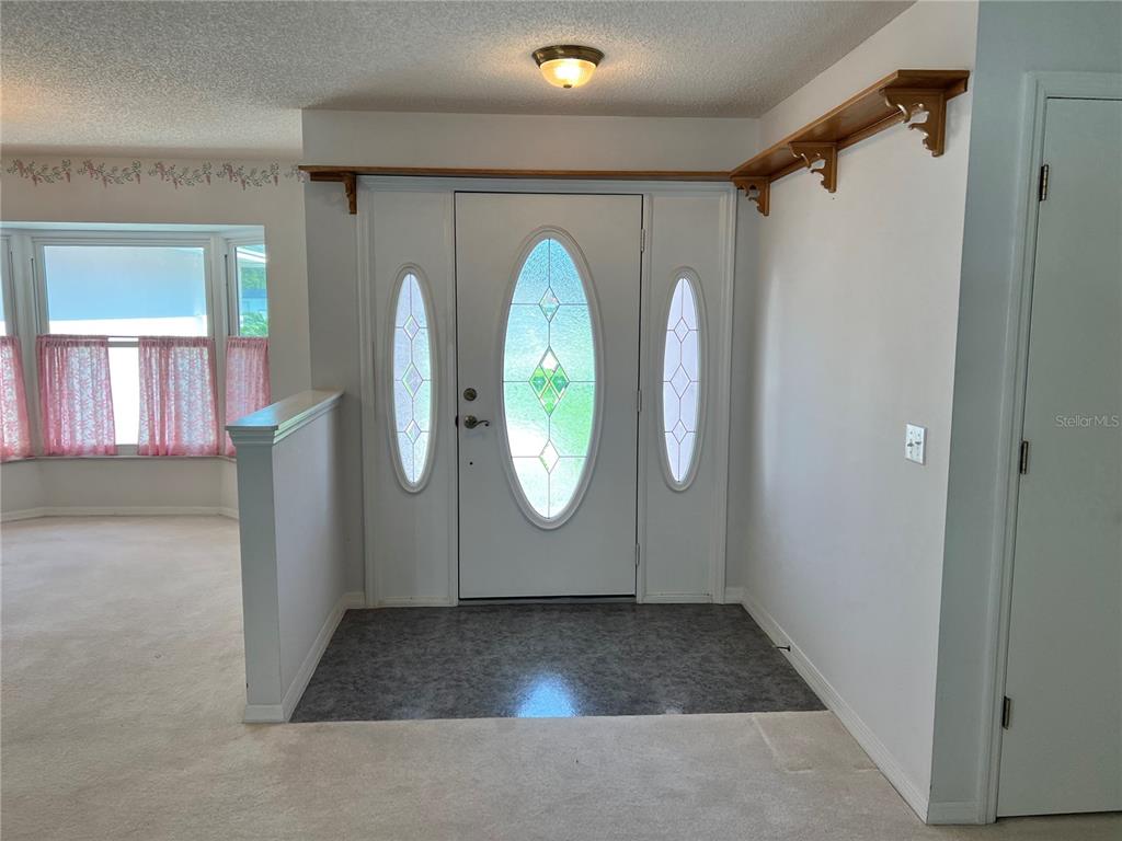 An entryway features a white front door with oval glass inserts, gray flooring, and shelving — 122 QUAILWOOD DRIVE, WINTER HAVEN, FL