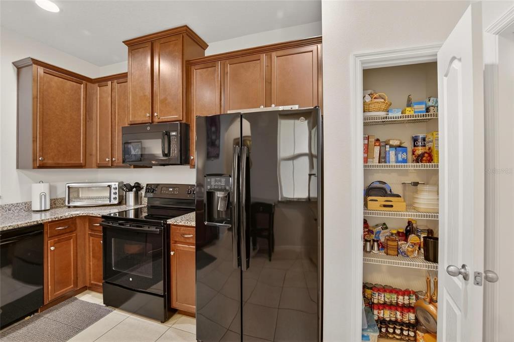 A kitchen features dark wood cabinets, black appliances, granite countertops, and an open pantry — 10808 VERAWOOD DRIVE, RIVERVIEW, FL