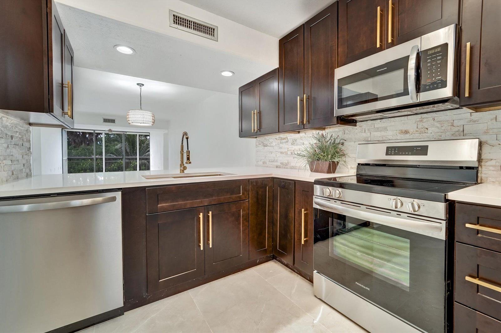 A kitchen features dark wood cabinets, stainless steel appliances, white countertops, and a stone backsplash — 6181 Balboa Circle # 303, Boca Raton FL 33433, BOCA RATON, FL
