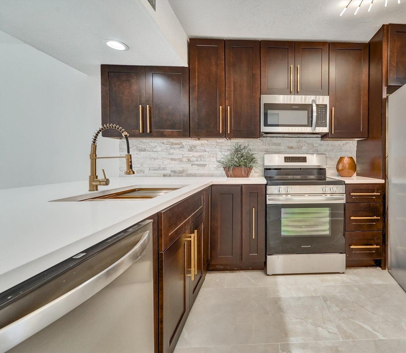 A kitchen featuring dark wood cabinets, white countertops, stainless steel appliances, and a stone backsplash — 6181 Balboa Circle # 303, Boca Raton FL 33433, BOCA RATON, FL