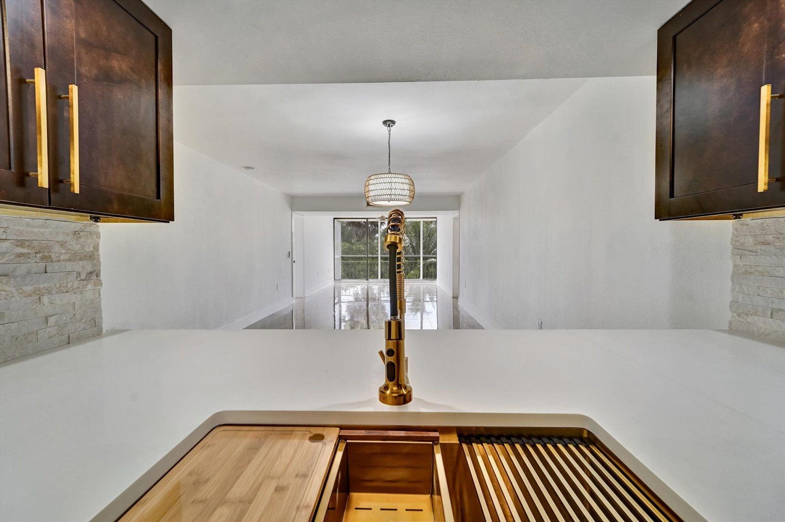 A kitchen sink with a gold faucet overlooks an empty living area with a balcony — 6181 Balboa Circle # 303, Boca Raton FL 33433, BOCA RATON, FL
