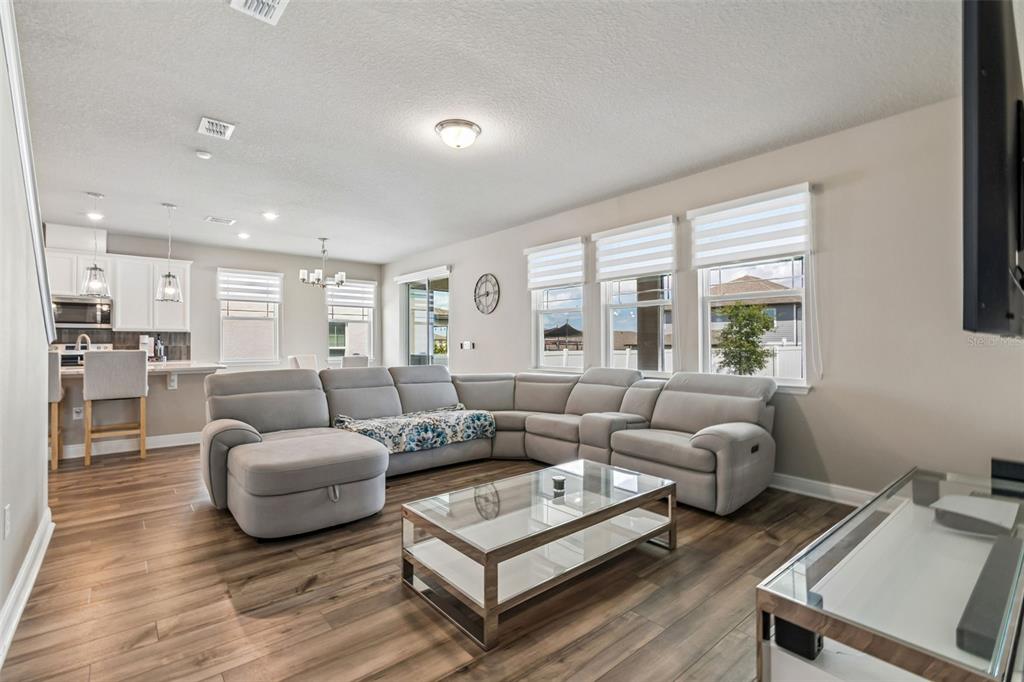 A living room with a large grey sectional, glass coffee table, and open-concept kitchen — 2310 RAVEN RIDGE ROAD, MINNEOLA, FL