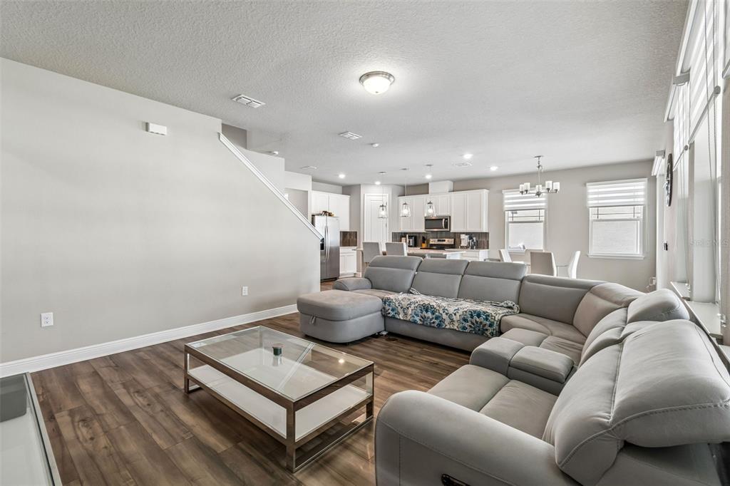 A living room with a large gray sectional sofa, glass coffee table, and open kitchen — 2310 RAVEN RIDGE ROAD, MINNEOLA, FL