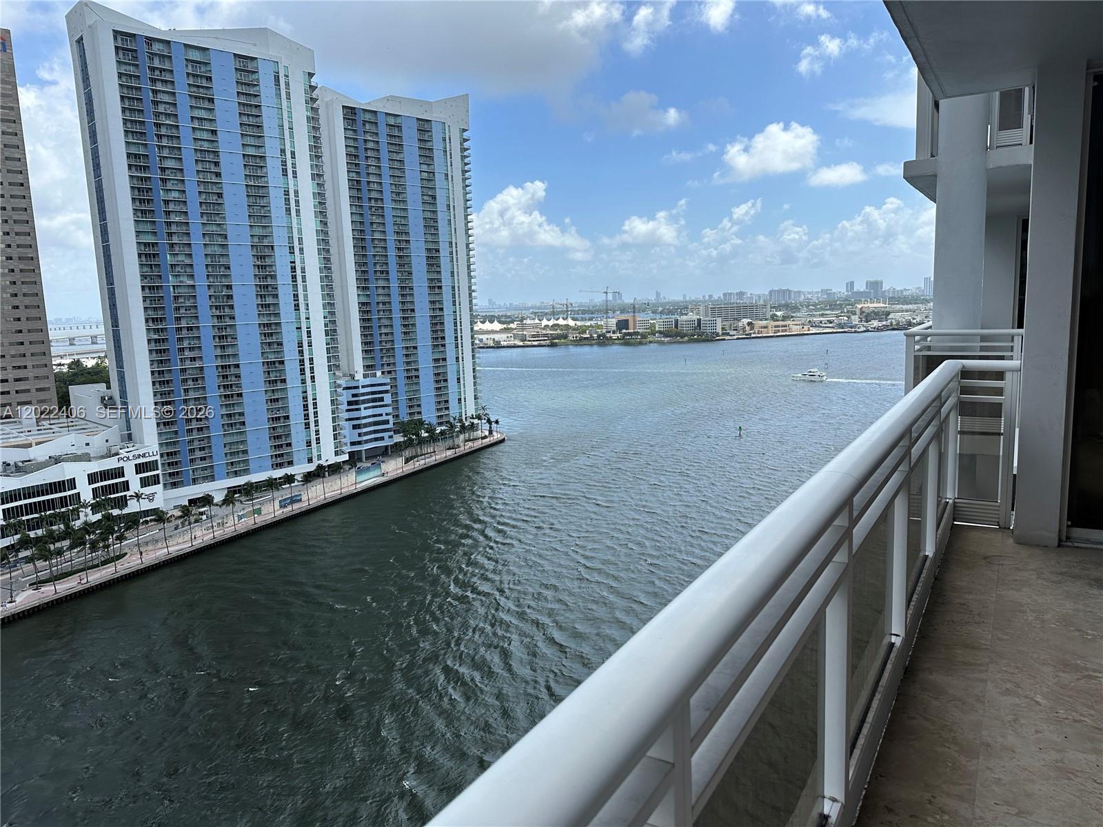 A high-rise balcony overlooks a wide river with a large blue residential building nearby — 901 Brickell Key Blvd # 2005, Miami FL 33131, MIAMI, FL