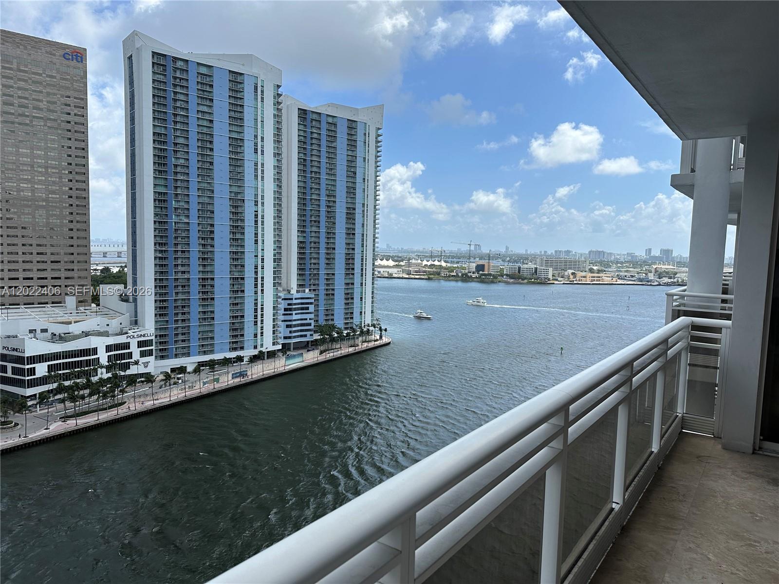 A high-rise balcony overlooks a river with large residential towers and a city skyline — 901 Brickell Key Blvd # 2005, Miami FL 33131, MIAMI, FL