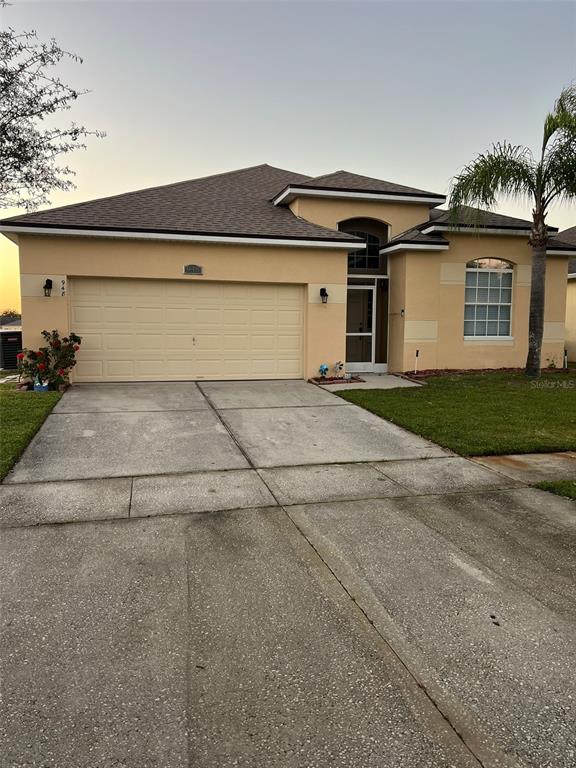 A single-story tan house with a two-car garage and a palm tree in the yard — 948 HACIENDA CIRCLE, KISSIMMEE, FL