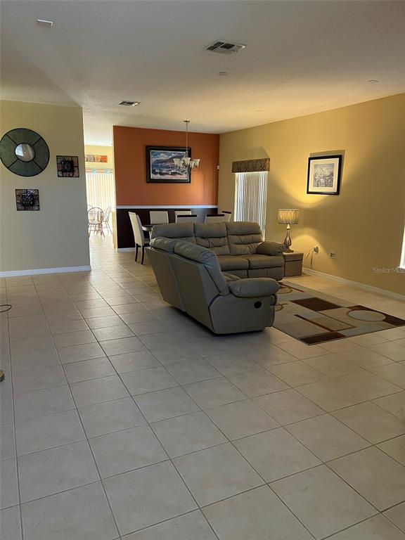 An open-concept living and dining area features tile flooring, neutral walls, and a leather sofa — 948 HACIENDA CIRCLE, KISSIMMEE, FL