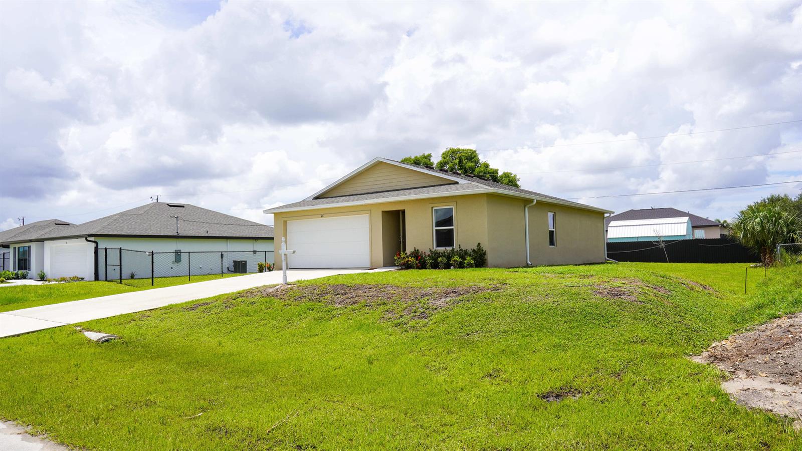 A single-story tan house with a white garage door sits on a grassy lot — 26 NE 12th Terrace, Cape Coral FL 33909, CAPE CORAL, FL