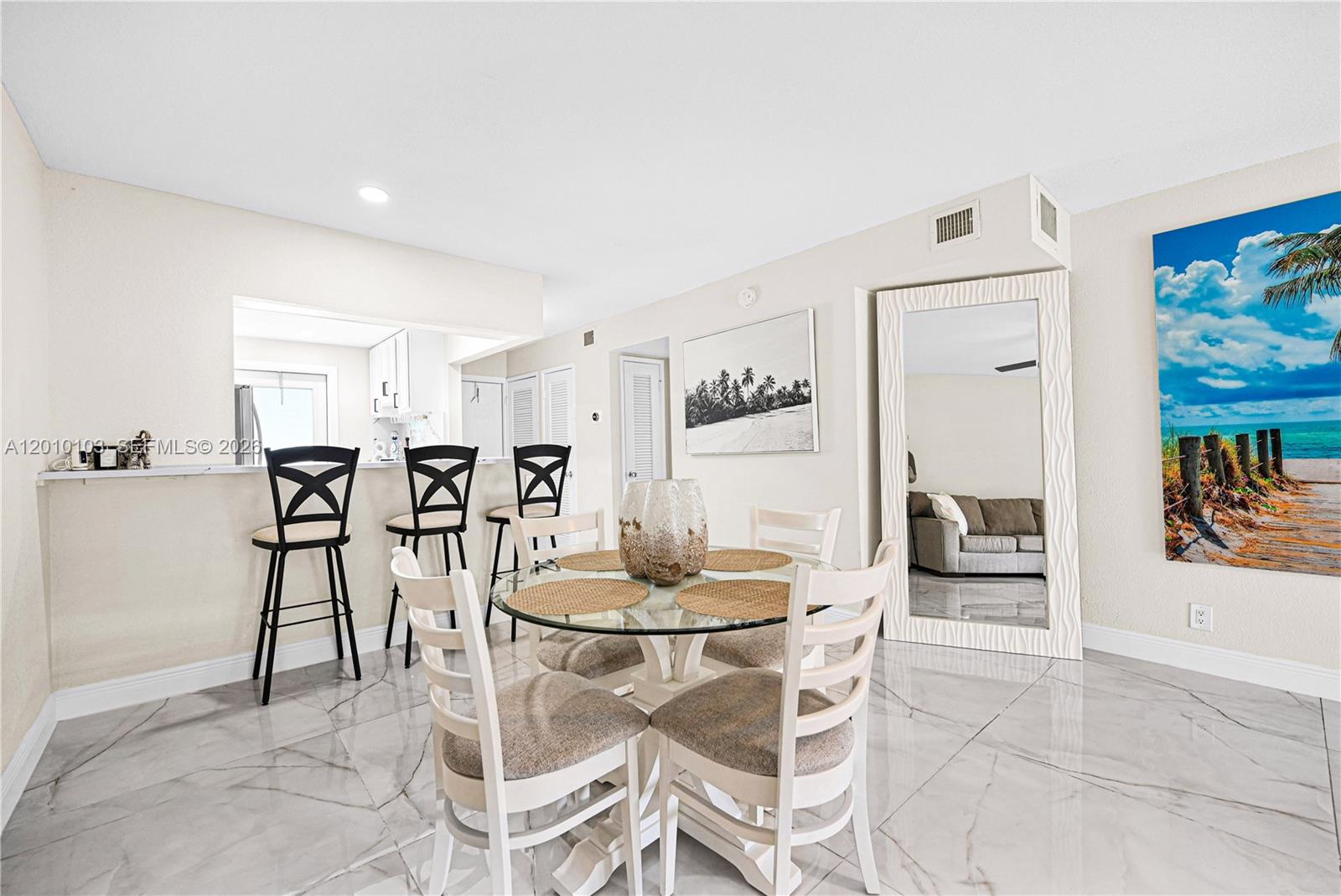 A dining area features a glass table, white chairs, bar stools, and a large mirror — 400 SE 10th St # 105, Deerfield Beach FL 33441, DEERFIELD BEACH, FL