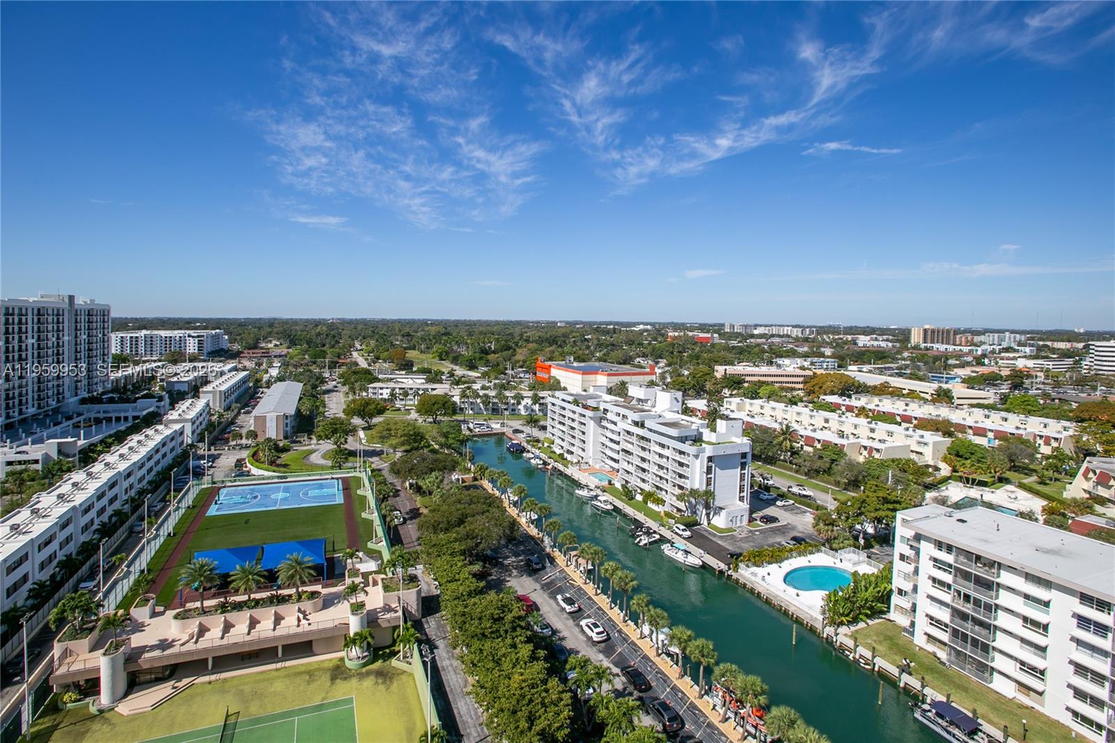 An aerial view shows a canal, apartment buildings, a tennis court, and a basketball court — 1800 NE 114th St # 1810, Miami FL 33181, MIAMI, FL