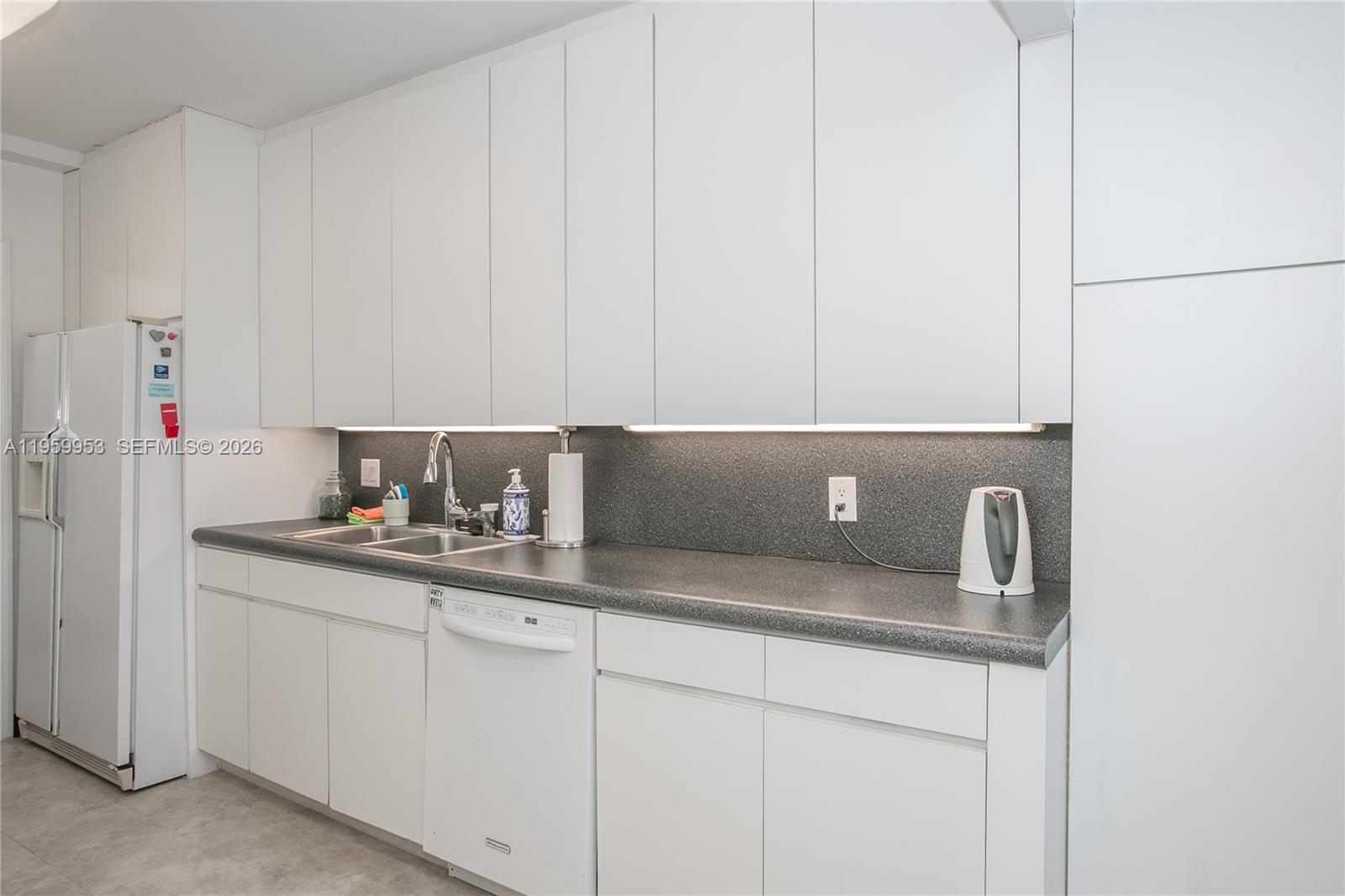 A kitchen features white cabinetry, a dark gray countertop, and a matching backsplash — 1800 NE 114th St # 1810, Miami FL 33181, MIAMI, FL
