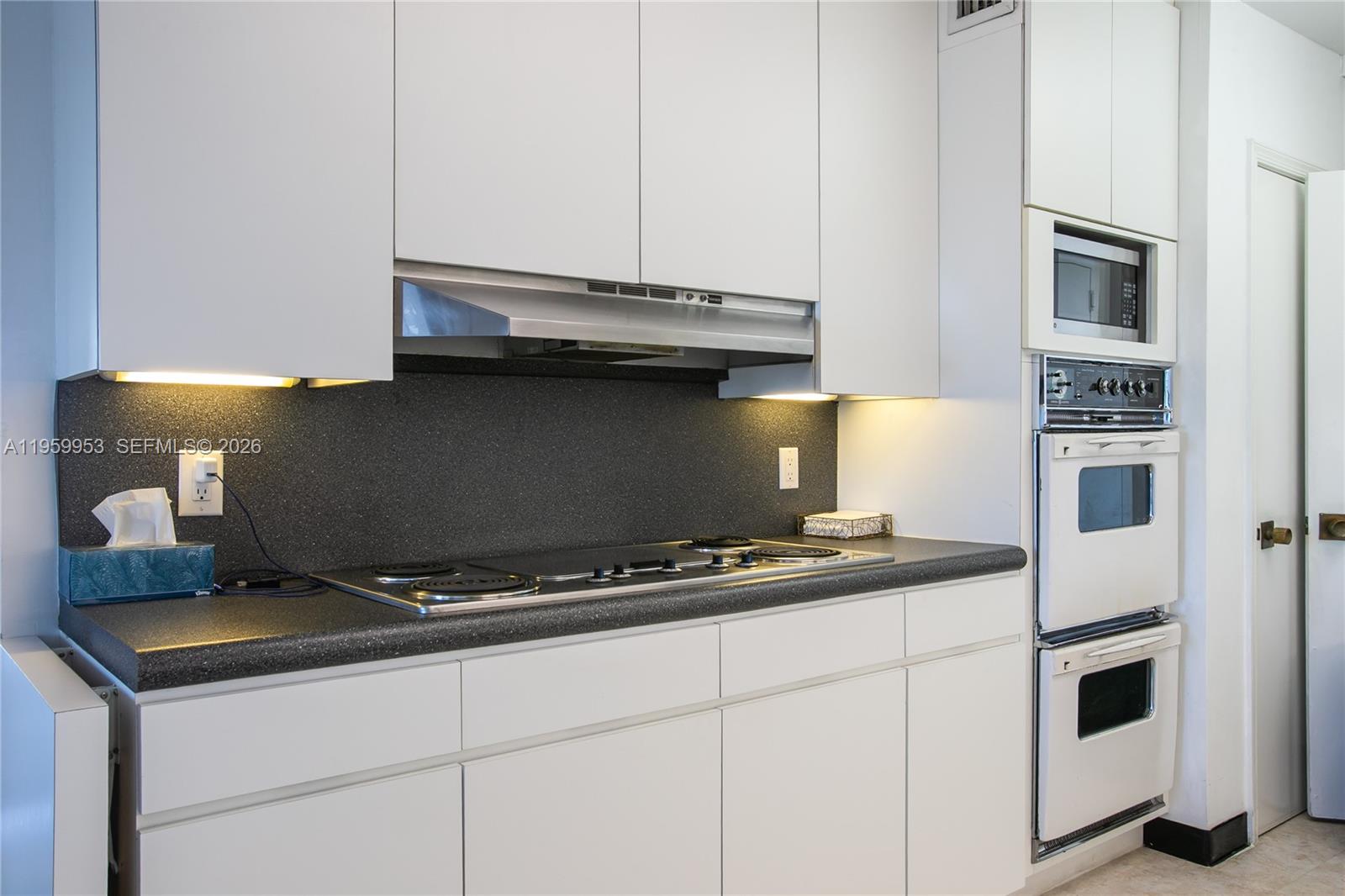 A kitchen features white flat-panel cabinets, a dark speckled countertop, and a built-in wall oven — 1800 NE 114th St # 1810, Miami FL 33181, MIAMI, FL