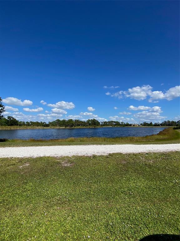 A gravel path leads to a lake surrounded by grass and trees under a blue sky — 119 WAHOO DRIVE, ROTONDA WEST, FL