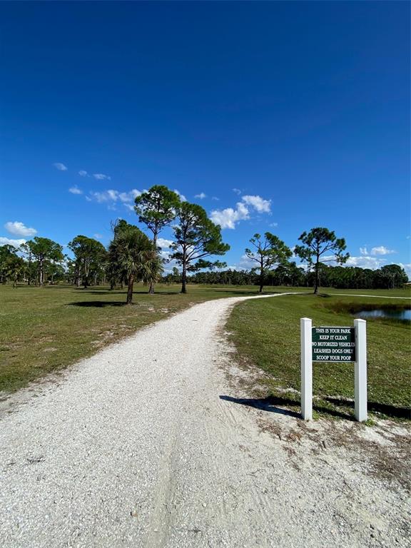 A gravel path winds through a grassy park area with scattered trees under a blue sky — 119 WAHOO DRIVE, ROTONDA WEST, FL