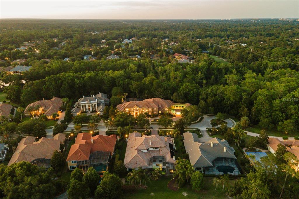 An aerial view shows several large houses with swimming pools surrounded by dense green trees — 3540 LEGACY HILLS COURT, LONGWOOD, FL