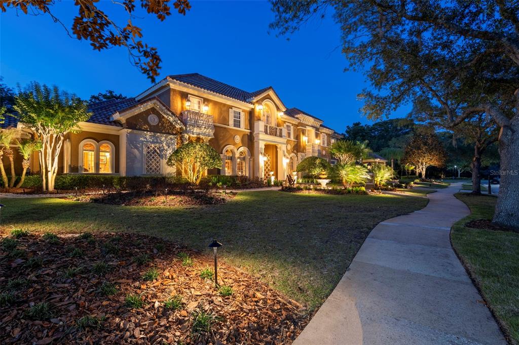 A large two-story Mediterranean-style house with a lit walkway and landscaping at dusk — 3540 LEGACY HILLS COURT, LONGWOOD, FL