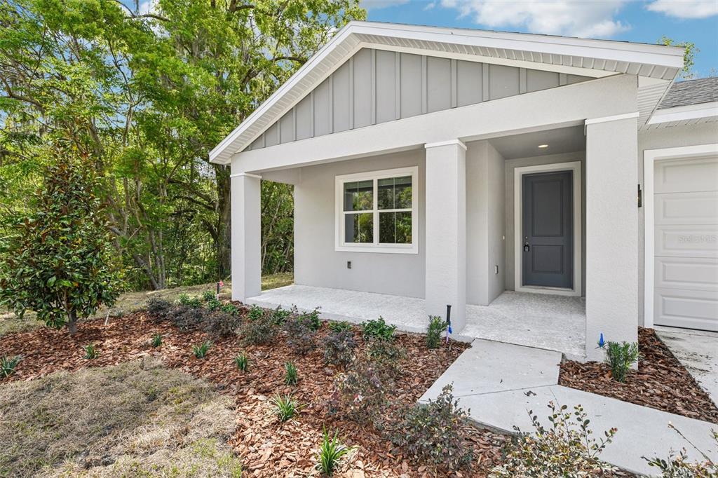 A gray one-story house exterior features a covered front porch, a dark door, and landscaping — 536 E BERESFORD AVENUE, DELAND, FL