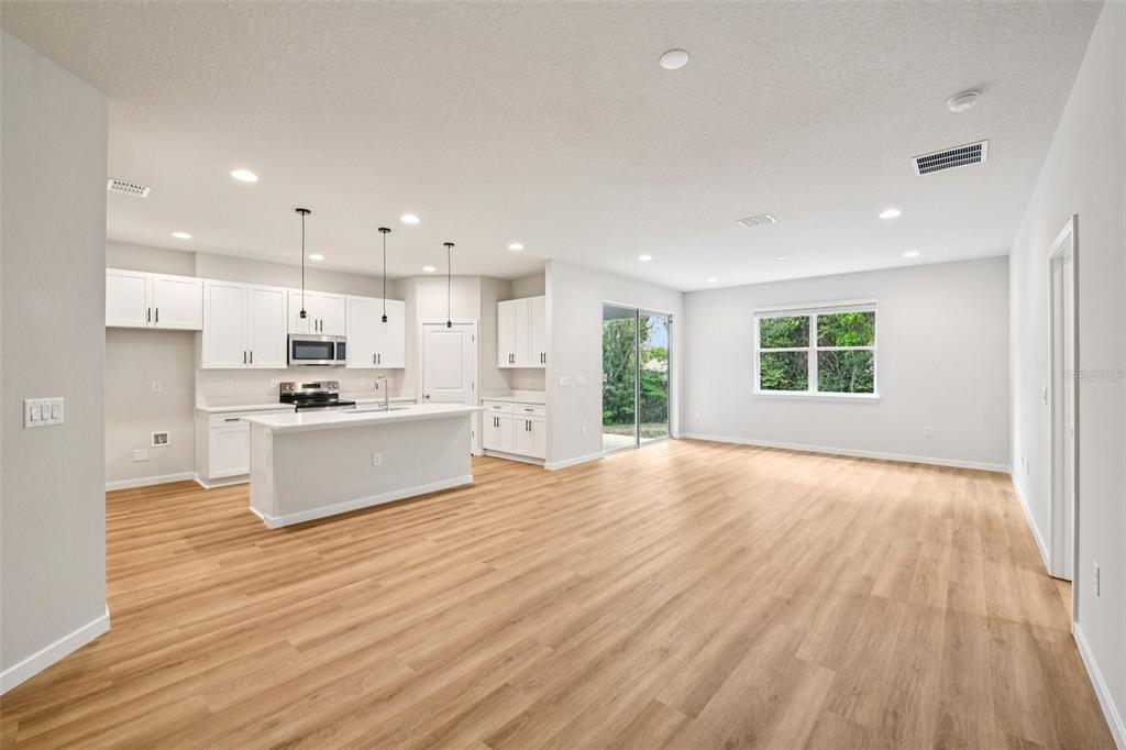 An open-concept kitchen and living area with white cabinets, a center island, and wood flooring — 536 E BERESFORD AVENUE, DELAND, FL