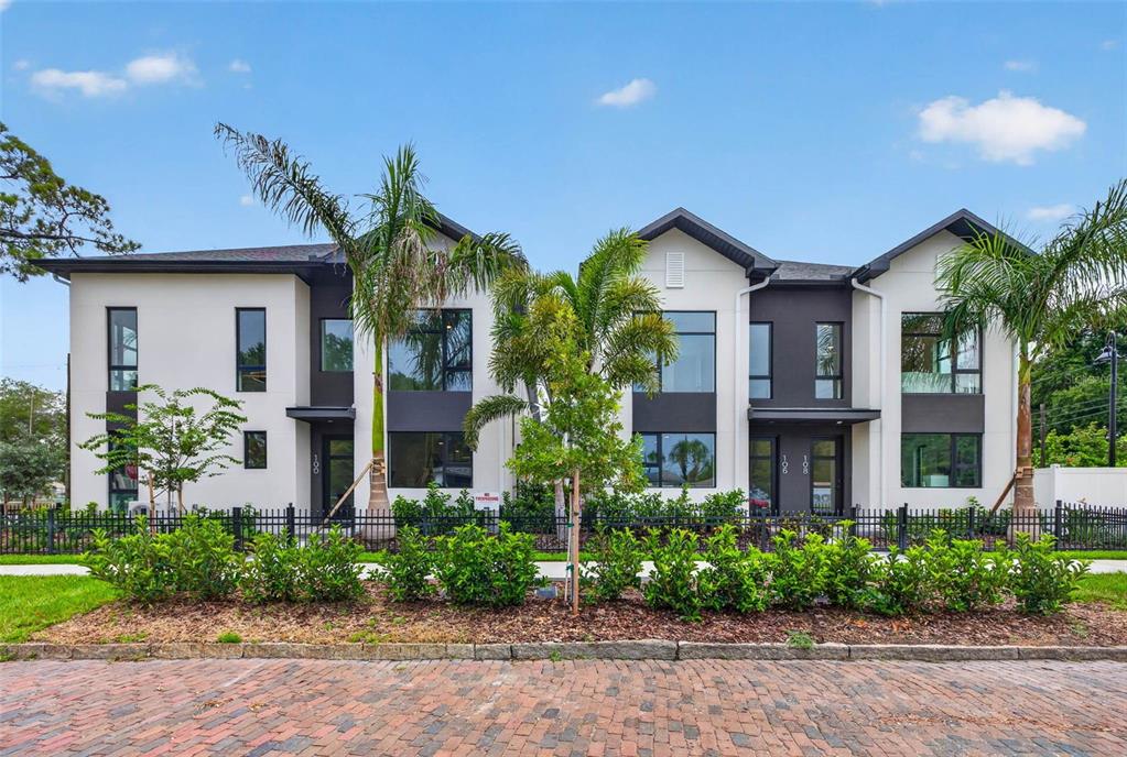 A modern three-unit townhouse complex features white and dark gray siding with palm trees — 108 36TH STREET N, ST PETERSBURG, FL