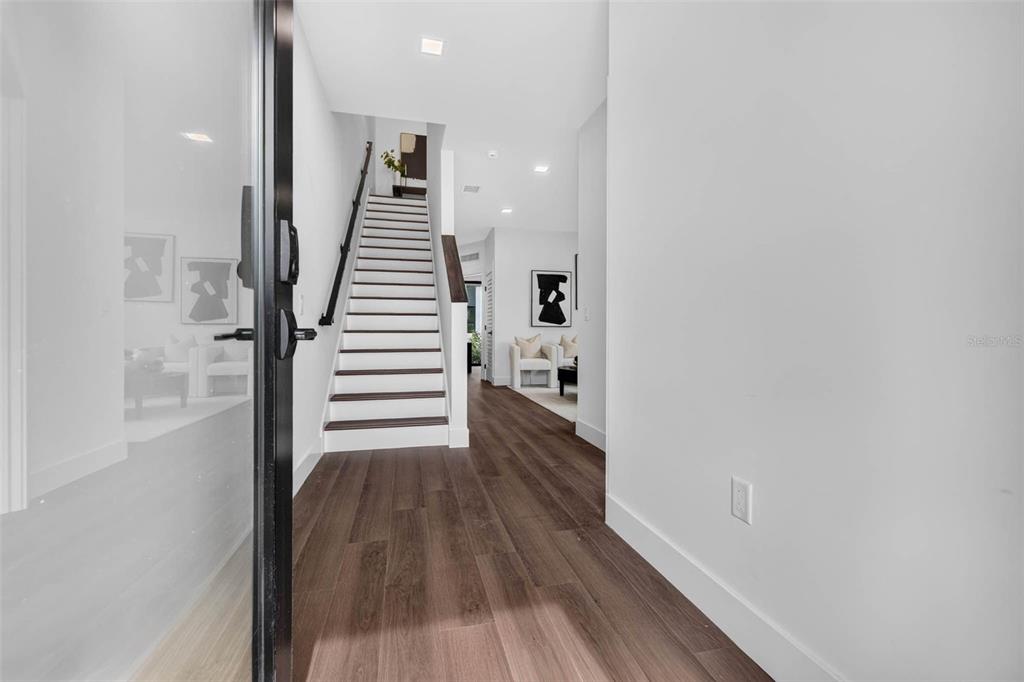 A modern entryway features wood-look flooring, a white staircase with dark treads, and recessed lighting — 108 36TH STREET N, ST PETERSBURG, FL