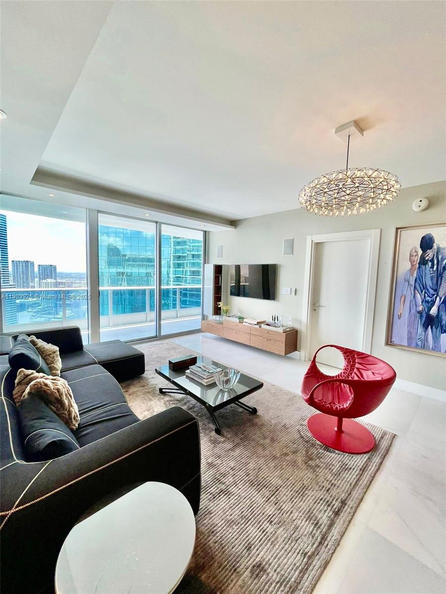 A modern living room features a dark sofa, red accent chair, and floor-to-ceiling windows — 200 BISCAYNE BOULEVARD WAY # 4310, Miami FL 33131, MIAMI, FL
