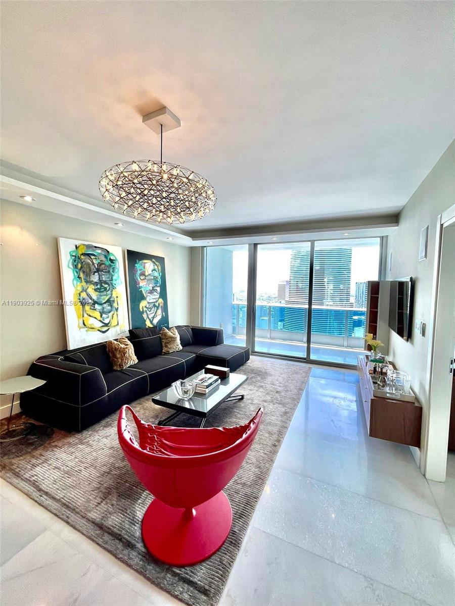 A modern living room features a black sectional sofa, a red accent chair, and floor-to-ceiling windows — 200 BISCAYNE BOULEVARD WAY # 4310, Miami FL 33131, MIAMI, FL