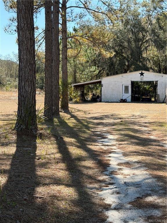 A white barn with an open garage bay sits on a sandy lot near trees — 10450 SW 60TH STREET, CEDAR KEY, FL