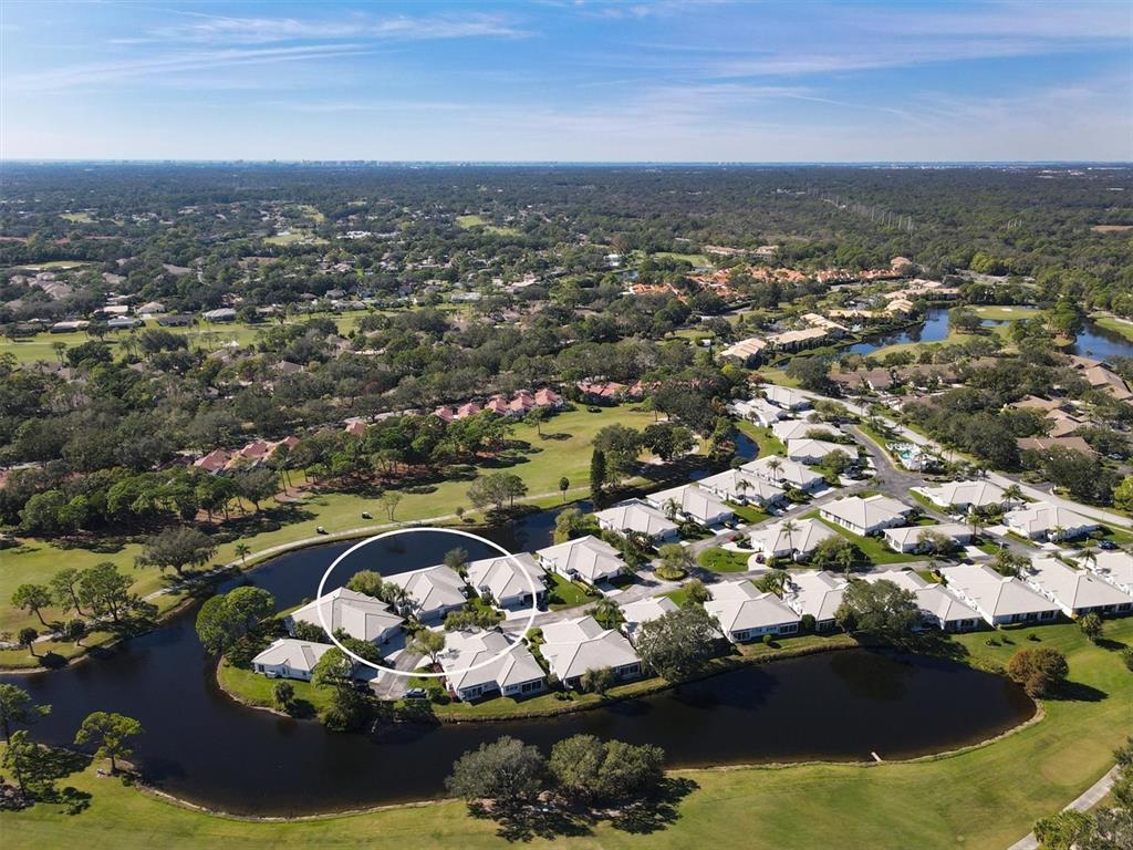 An aerial view shows a residential community with houses situated along a winding pond — 5662 LONG COMMON CIRCLE UNIT 8, SARASOTA, FL