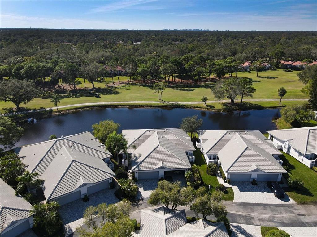 An aerial view shows several houses with gray tile roofs situated along a small lake — 5662 LONG COMMON CIRCLE UNIT 8, SARASOTA, FL