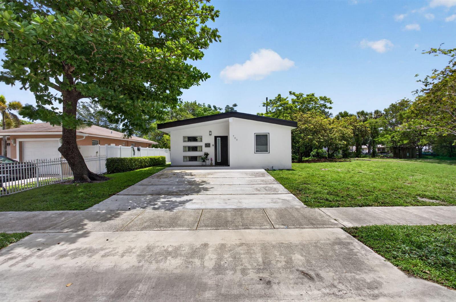 A white, single-story house with a flat roof and a concrete driveway sits on a lawn — 700 NW 17th Terrace, Pompano Beach FL 33069, POMPANO BEACH, FL