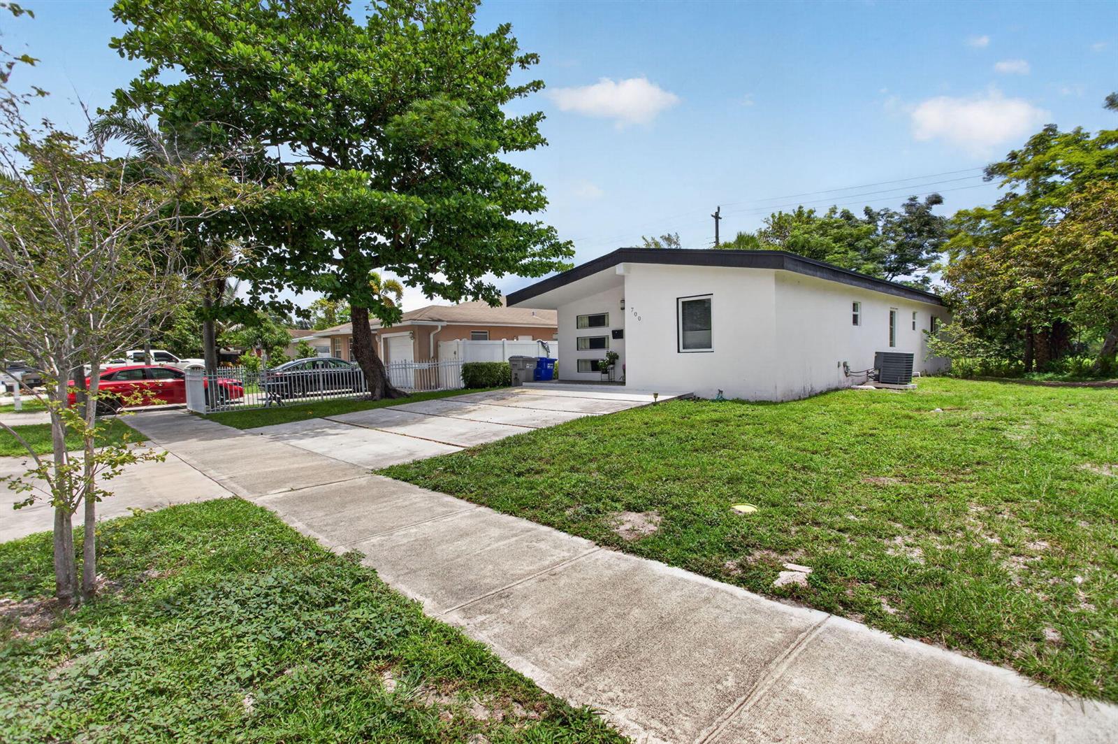 A single-story white house with a flat roof and a concrete driveway sits on a lawn — 700 NW 17th Terrace, Pompano Beach FL 33069, POMPANO BEACH, FL