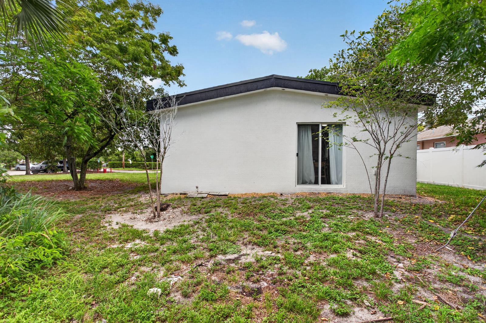 The exterior of a white, single-story house features a sliding glass door and surrounding trees — 700 NW 17th Terrace, Pompano Beach FL 33069, POMPANO BEACH, FL