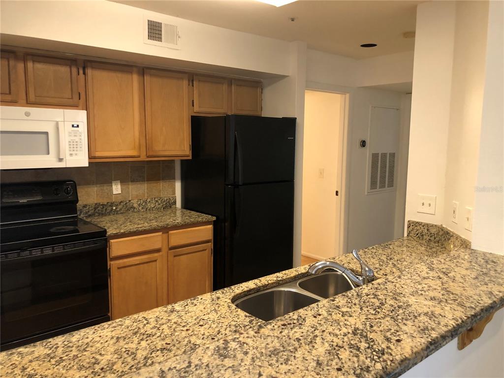 A kitchen features wood cabinets, granite countertops, a black refrigerator, and a double-basin sink — 482 N PIN OAK PLACE UNIT 308, LONGWOOD, FL