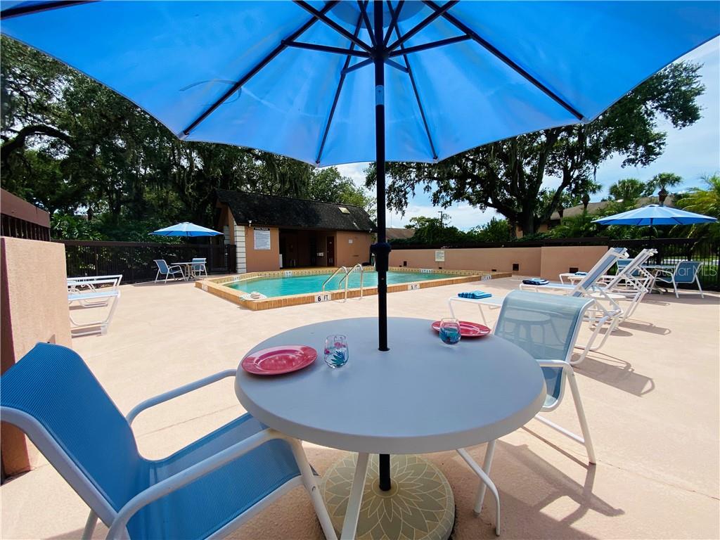 A patio table and chairs sit under a blue umbrella by a swimming pool — 1515 FORREST NELSON BOULEVARD UNIT C202, PORT CHARLOTTE, FL