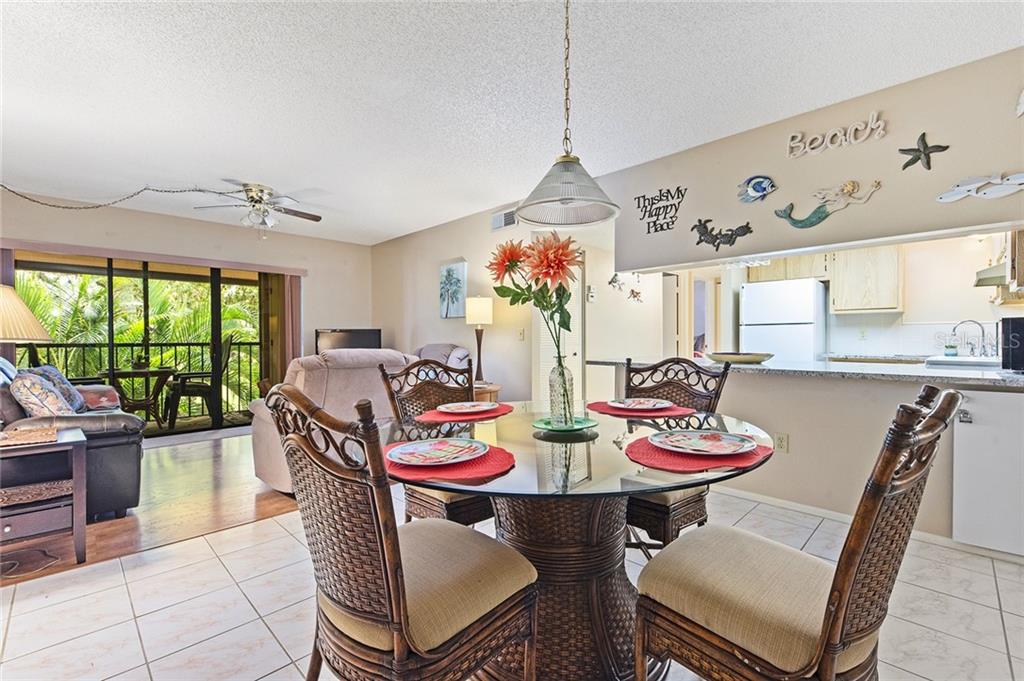 A dining area with a glass table and wicker chairs opens to a living room — 1515 FORREST NELSON BOULEVARD UNIT C202, PORT CHARLOTTE, FL