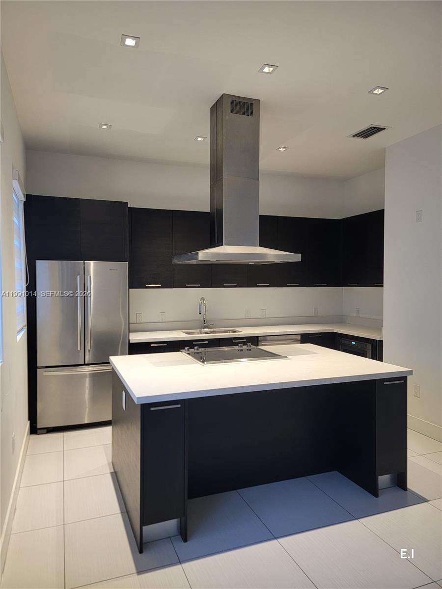 A modern kitchen features dark cabinetry, a white island with a cooktop, and stainless appliances — 9133 NW 33rd St, Doral FL 33172, DORAL, FL