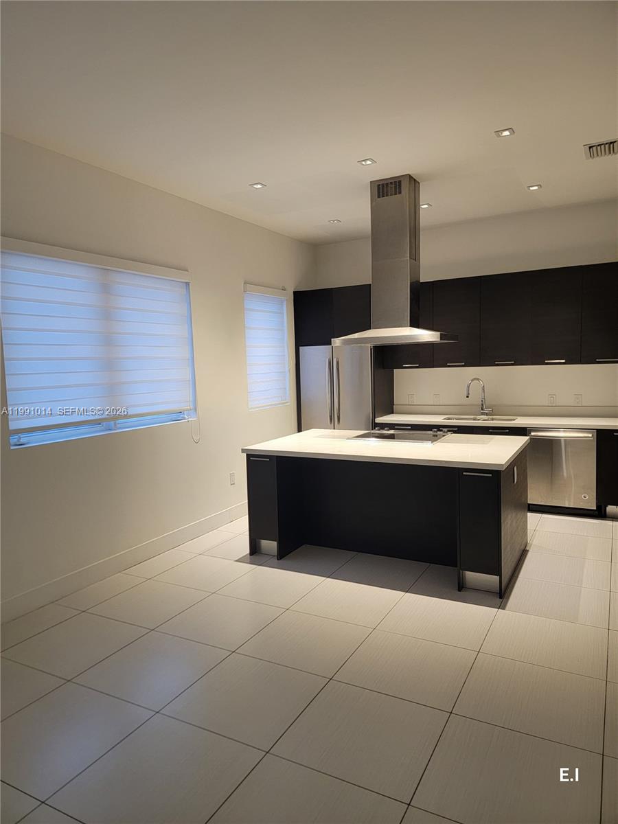 A modern kitchen features dark cabinetry, a central island with a cooktop, and tile flooring — 9133 NW 33rd St, Doral FL 33172, DORAL, FL