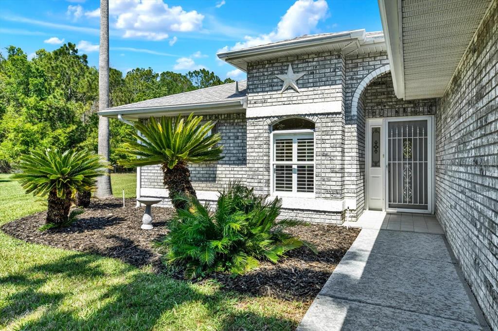 A gray brick house features a front entrance with a white door and a star decoration — 29451 SCHINNECOCK HILLS LANE, SAN ANTONIO, FL