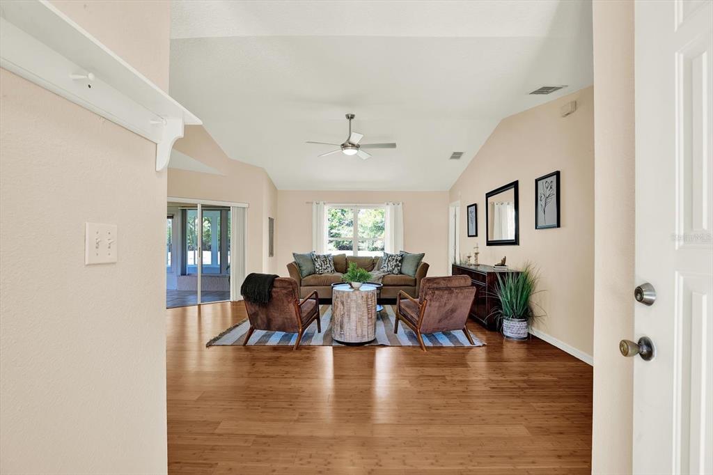 A living room with wood flooring, a vaulted ceiling, and a seating area — 29451 SCHINNECOCK HILLS LANE, SAN ANTONIO, FL